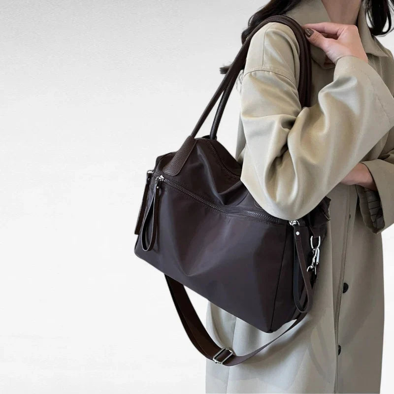 Sac à main NARA café en toile résistante, léger et pratique, avec bandoulière ajustable, offrant grande liberté de mouvement pour vos essentiels du quotidien, porté épaule.