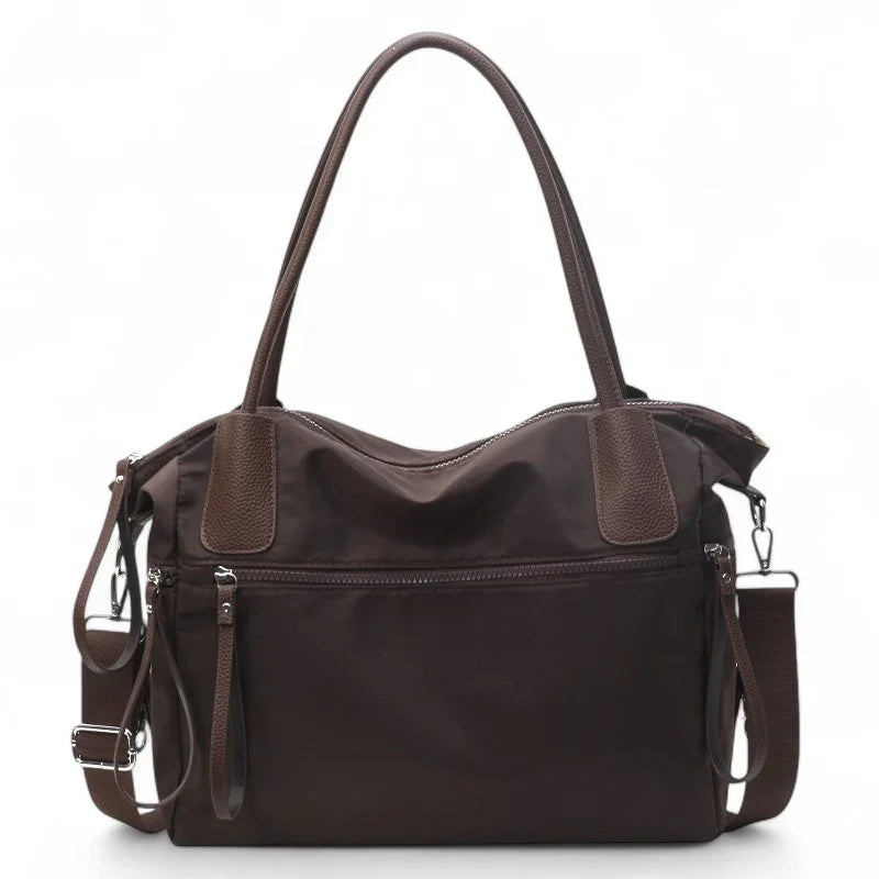 Sac à main NARA café en toile résistante, léger et pratique, avec bandoulière ajustable, offrant grande liberté de mouvement pour vos essentiels du quotidien.